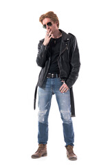 Cool serious young biker or rocker with sunglasses in leather jacket smoking cigarette look down....