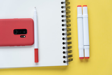 High angle shot of a journal, marker pens, and a smartphone on a yellow background