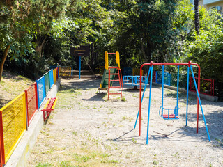 Fototapeta na wymiar Children's playground with swings and a slide surrounded by a multicolored fence and green trees