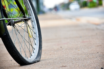 Rear wheel of bike which is flat and parked on the pavement beside the road.