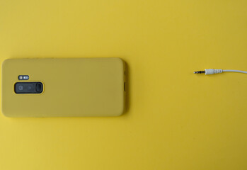 High angle shot of a smartphone with a yellow case and a power connector on a yellow background