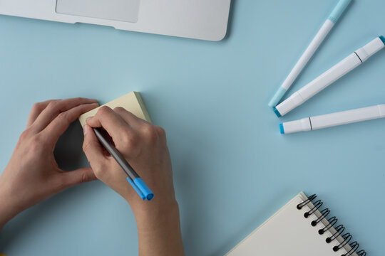 High Angle Shot Of A Person Writing On Sticky Notes And A Journal, Pens, And Laptop On The Table