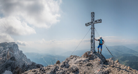 Mountaineer standing next to a summit cross on a mountain peak