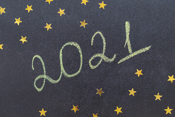 Fototapeta na wymiar Christmas and New Year concept. Chalk handwritten inscription 2021 on a black board. With golden stars. 