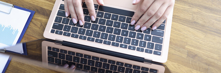 Fototapeta na wymiar Female hands are typing on laptop keyboard at table in office closeup. Remote work at home concept.