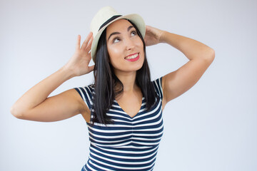 Young beautiful woman wearing straw hat and striped t-shirt smiling over white background.