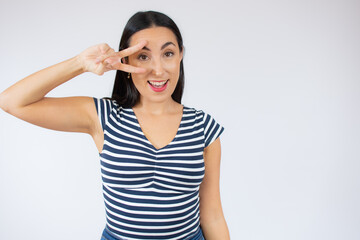 Portrait of gorgeous brunette woman in striped t-shirt looking at camera with smile and showing peace sign with fingers isolated over white background