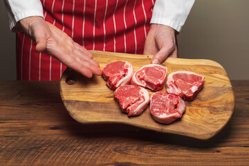 Professional butcher in classic red and white apron holding cutting board with fresh uncooked lamb loin chops. Meat industry product and concept