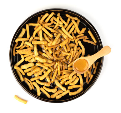 An isolated image of a pile of some bread sticks or cracker sticks on a plate with honey and a spoon on a white plate or table top. Spicy appetizer close-up image on a white background.