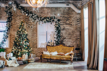 The loft-style room is decorated with New Year's decorations. Luxurious vintage leather sofa and Christmas tree.
