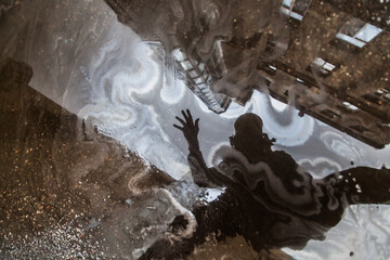 Silhouette of man reflected in puddle with oil slick