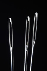 three sewing needles without thread on a dark background. macro.