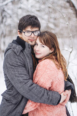 Fototapeta premium A couple - a man with glasses and a young girl in winter clothes hugging in a winter forest