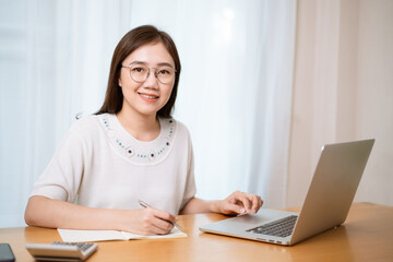 Young Asian happy woman using her personal laptop computer for working and making a video conference with her friend and colleague. 