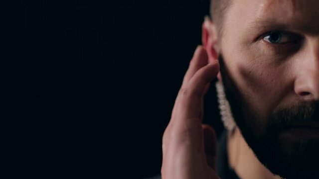 Half of face of bearded security listening someone through earphone while standing over black background. Protection and confidence concept.