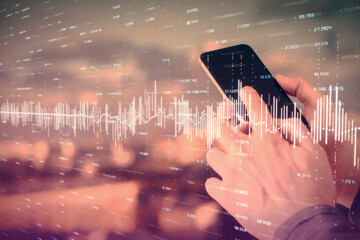 Double exposure of man's hands holding and using a digital device and forex graph drawing. Financial market concept.