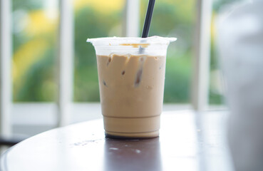 Iced coffee in a plastic cup with a straw that is still half a glass on the table