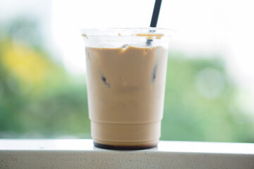 Iced coffee in a plastic cup with a straw that is still half a glass on the table
