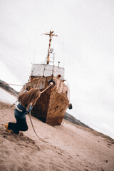 a girl drags on a rope drags a ship that was thrown onto the beach