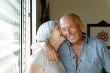 bellissima coppia di anziani si abbraccia felice vicino alla finestra del salotto