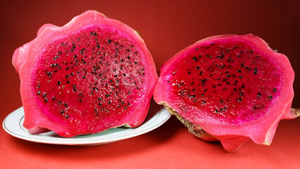 Close up of red dragon fruit slice on a white galss plate on a red background. healthy and fresh...