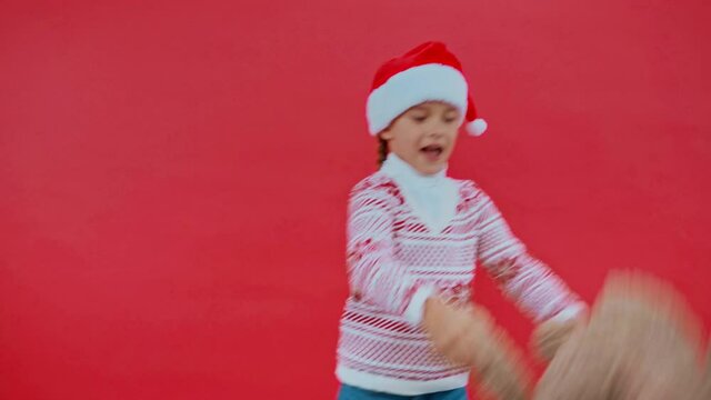 girl in santa hat and christmas sweater dancing with teddy bear isolated on red