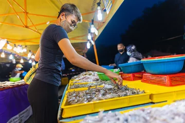 Outdoor kussens Street food night market at  Putrajaya, near Kuala Lumpur. Young asian girl buys seafood in a night market. Malaysian women with face mask in a street market © Holger