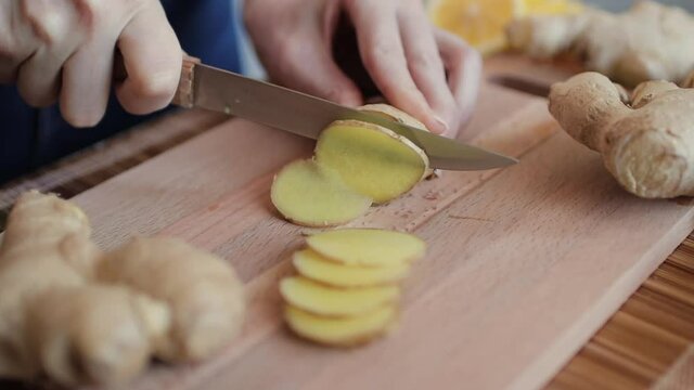 Woman cutting fresh ginger root on kitchen table, close up