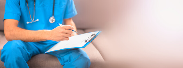 A doctor in a blue uniform with a stethoscope sitting on the couch records anamnesis or prescribes a course of treatment. Pastel colors are a place for your text - obrazy, fototapety, plakaty
