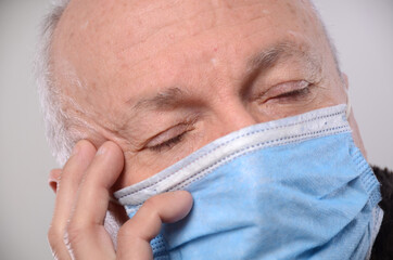  Senior man in medical facemask suffering from headache