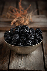 Fresh blackberry in vintage copper bowl on natural wooden background.