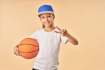 Adorable girl holding basketball ball and showing victory gesture