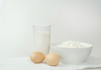 On the table a glass of milk, two eggs and cottage cheese on a light background