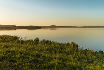 beautiful lake landscape at sunset. green grass, water and clear sky at sunset