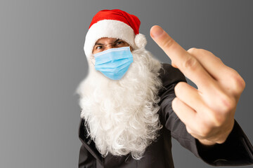 Bad brutal funny old bearded angry naughty bad Santa Claus wearing costume, glasses, face mask showing middle finger hand gesture isolated on Christmas red background. Stop Covid 19 concept.