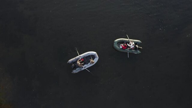 The frame vertically from top to bottom shows the water surface on which two inflatable rowboats are drifting, people in boats on an evening walk lightly row their oars and move in a circle.