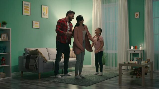 Dad and child are rotating mom with eyeband and on her head, to play funny game, preferring to spend weekend evening at home, enjoying time in family circle, Slow motion.