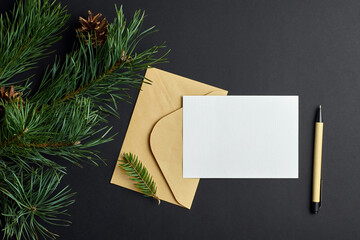Christmas greeting card mockup with envelope, pen and pine tree branch with cones on black background