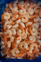 Many frozen shrimp are in an open box. Factory standard blue seafood packaging. Top view, vertical format. Frozen shrimp background. Seafood