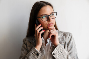 Beautiful thinking businesswoman in eyeglasses talking on cellphone