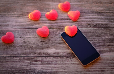 Red hearts and black smart phone with blank screen on old wooden background, online communication daiting concept, selective focus