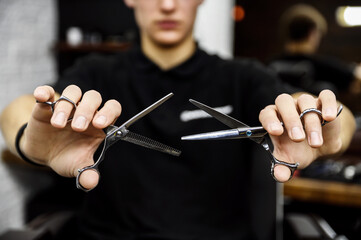 hairdresser holding stylish black hairdressing scissors for cutting models in front of him pair of scissors in the hands of a barber scissors on the background of a man barber accessories haircut 