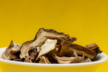 a bunch of dried porcini mushrooms, in a white saucer on a yellow background with a shadow pattern