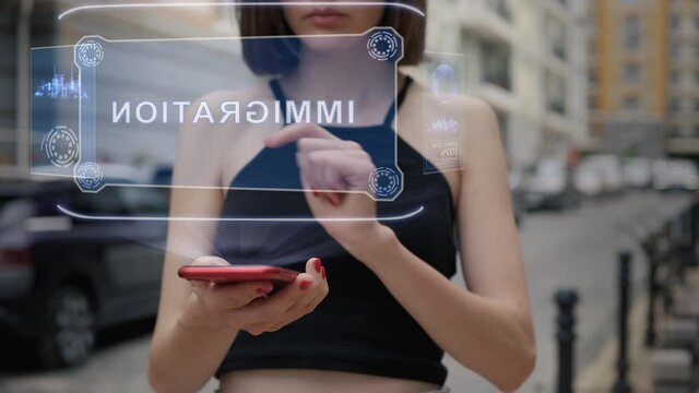 Unrecognizable young adult woman standing on the street interacts HUD hologram with text Immigration. Girl in black clothes uses technology of the future mobile screen