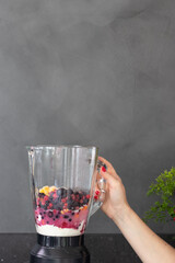 Woman holding a mixer full of fruits, carrot and yogurt on a gray background, preparing healthy smoothie full of vitamines