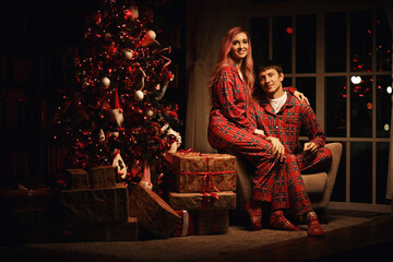 a man and a woman in red pajamas are sitting at night near the christmas tree
