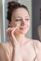 The girl applies cream to her face. Skin care at home in the bathroom.