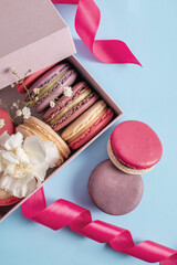 Multicolored macarons in a pink box on a blue background. Birthday present, sweet biscuits. Copy space