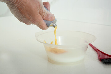 Woman preparing dye for hair coloring at white table, closeup