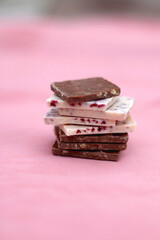 Stack of dark and white chocolate pieces. Selective focus, pink background.